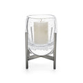 Clear glass hurricane with cream pillar candle inside, supported by stainless steel stand with cross-base design.