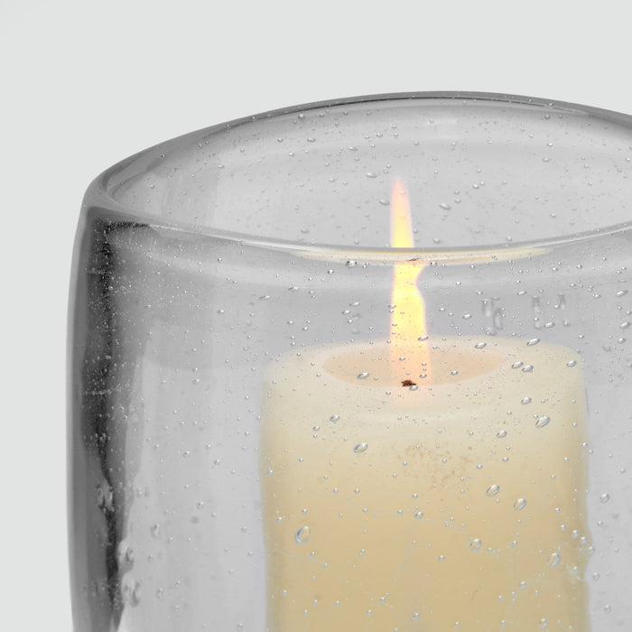 Clear glass hurricane with textured surface and lit cream-colored candle inside.