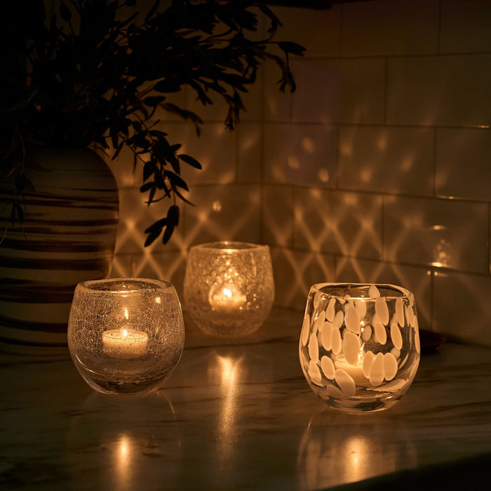 Three lit tealight candles in textured glass holders with geometric patterns, casting warm light and shadows.