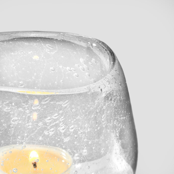 Clear glass tealight holder with textured surface and yellow tealight candle burning inside.