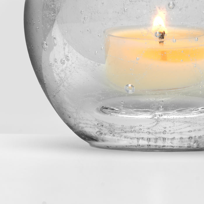 Lit cream-colored tealight in textured glass holder with water droplets and bubbles on surface.