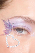 Close-up of an eye adorned with a purple glitter butterfly temporary tattoo and a heart-shaped rhinestone design below.