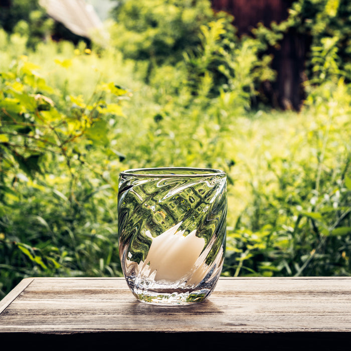 Clear glass candle with swirled pattern sitting on wooden surface outdoors.