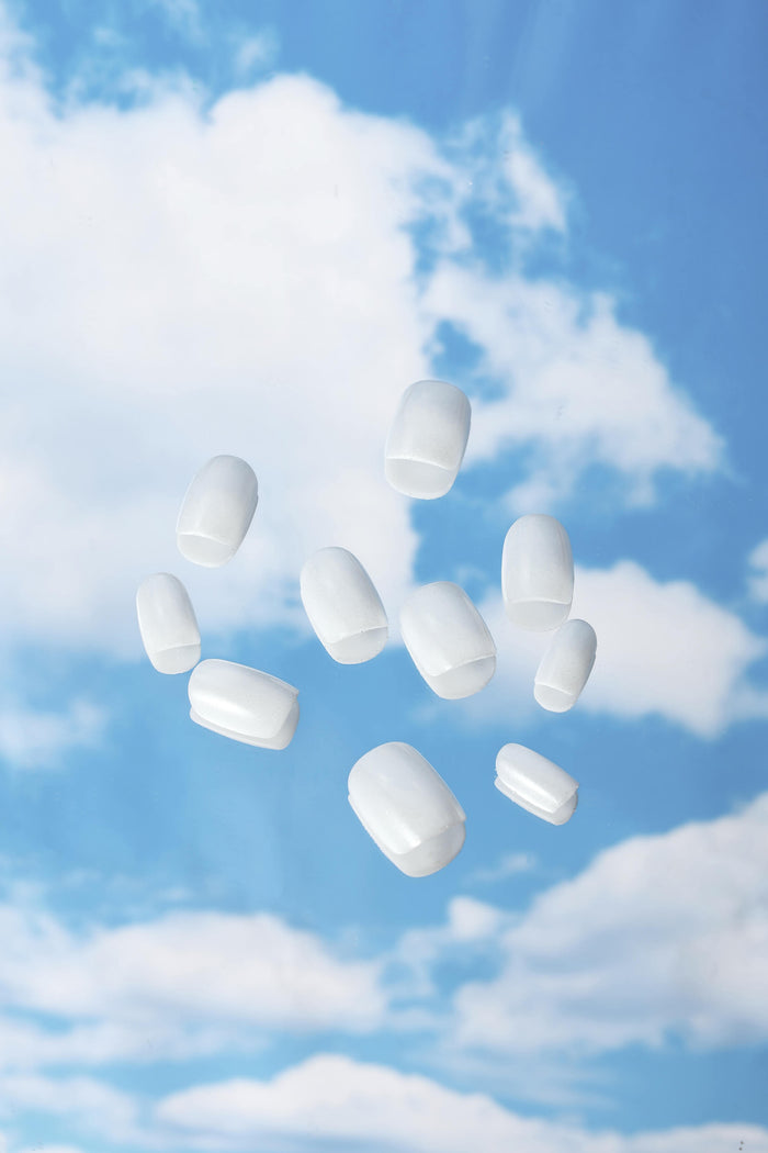 Clean white square press-on nails floating against a blue sky with clouds, representing casual chic style.