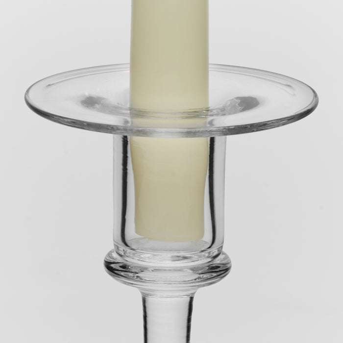 Clear glass candlestick with wide circular drip pan holding a cream pillar candle.