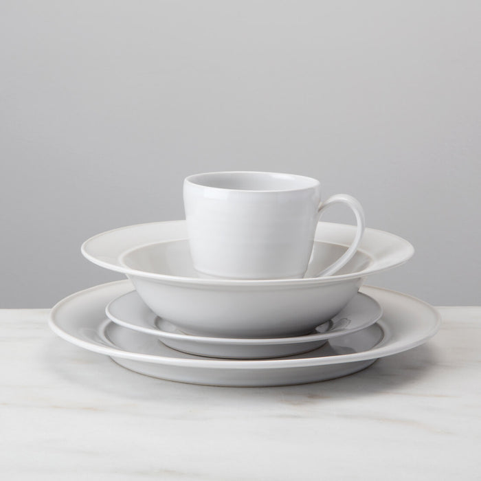 White ceramic dinnerware set stacked with plates, bowl, and cup with handle.