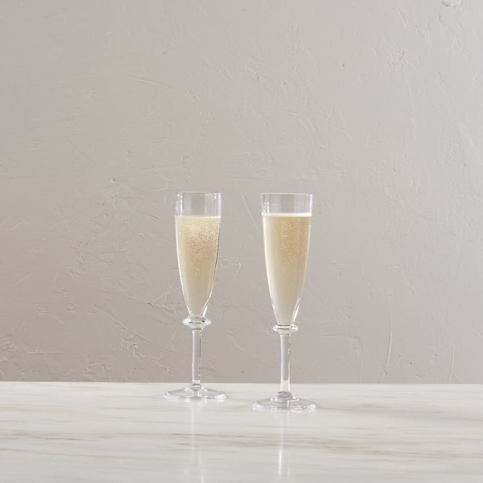 Two clear champagne flutes filled with sparkling wine on a white surface.