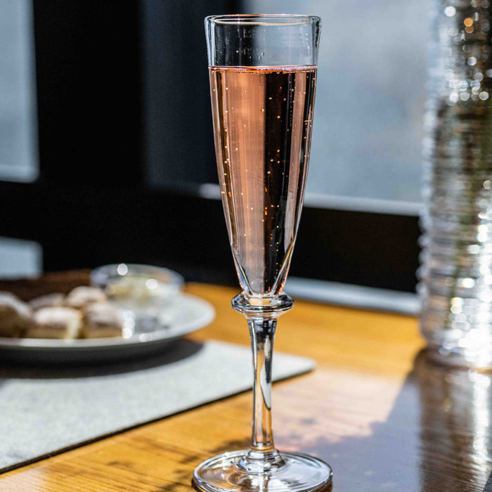 Tall champagne flute filled with sparkling rosé wine on wooden table with place setting.