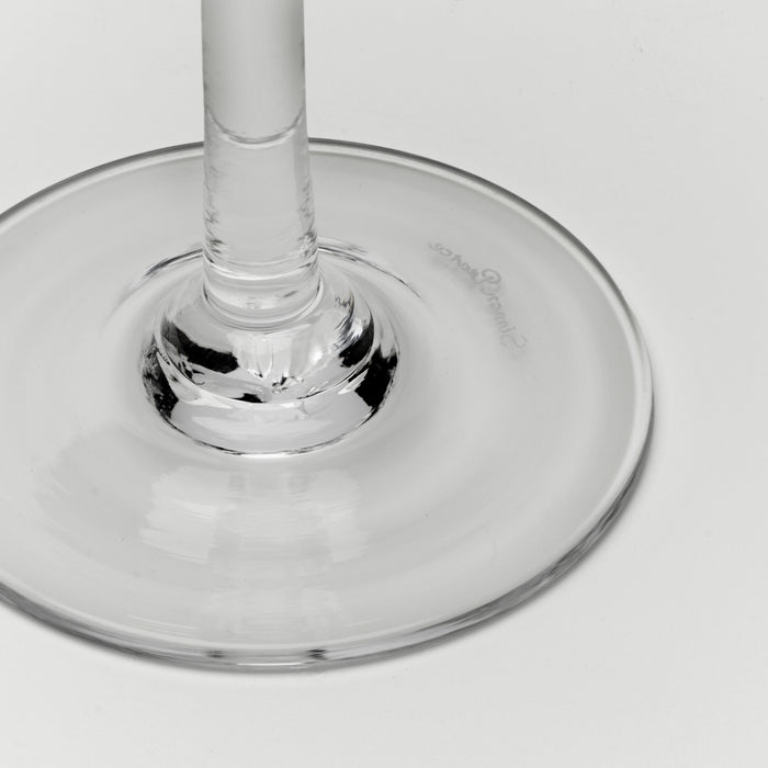 A close-up of a clear glass wine glass base and stem on a light gray background.