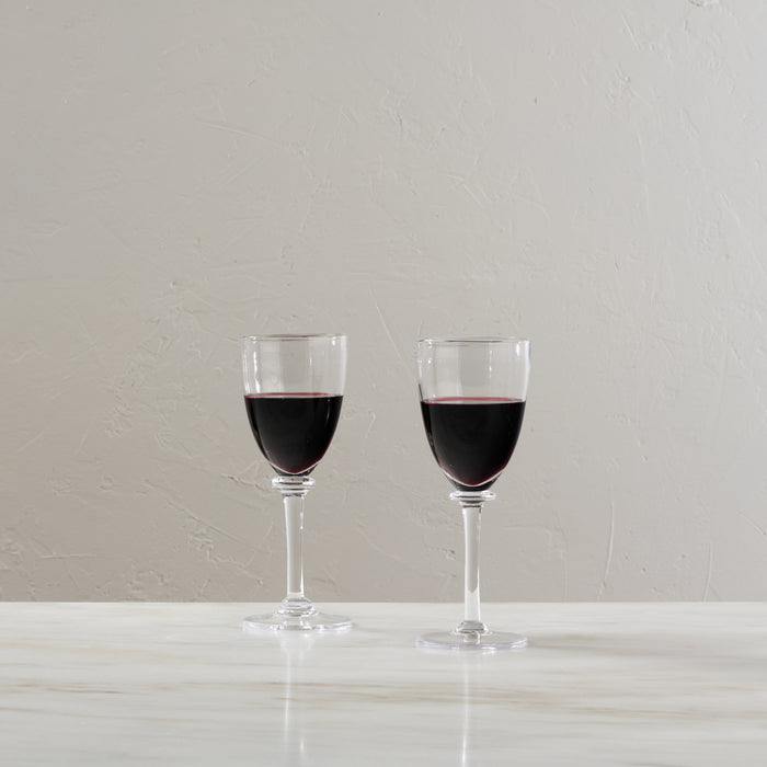 Two glasses filled with dark red wine on a white surface against a neutral background.