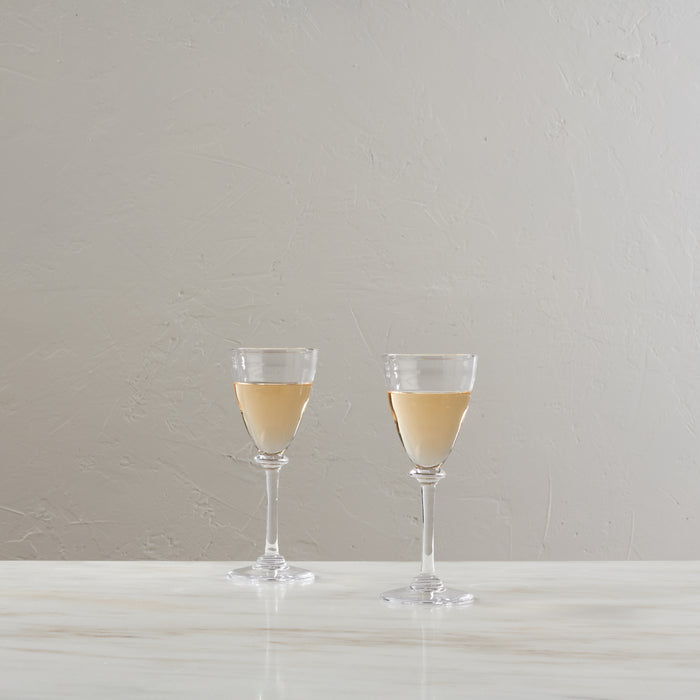 Two wine glasses filled with pale yellow white wine on a white surface against a neutral background.