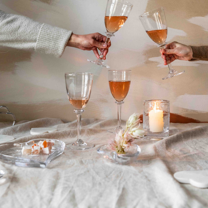 Two hands holding wine glasses filled with amber-colored wine on a neutral-toned table setting.