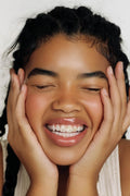 Close-up of a smiling young woman with celestial-themed tooth gems on her teeth: a moon, stars, and a sun.