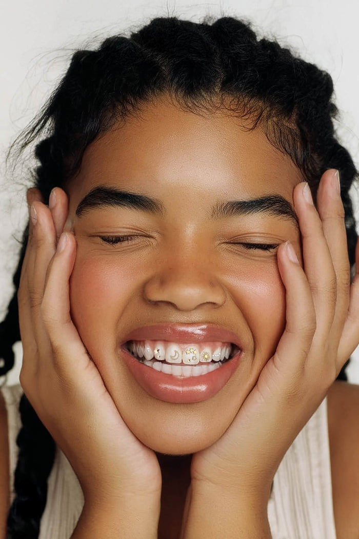 Close-up of a smiling young woman with celestial-themed tooth gems on her teeth: a moon, stars, and a sun.