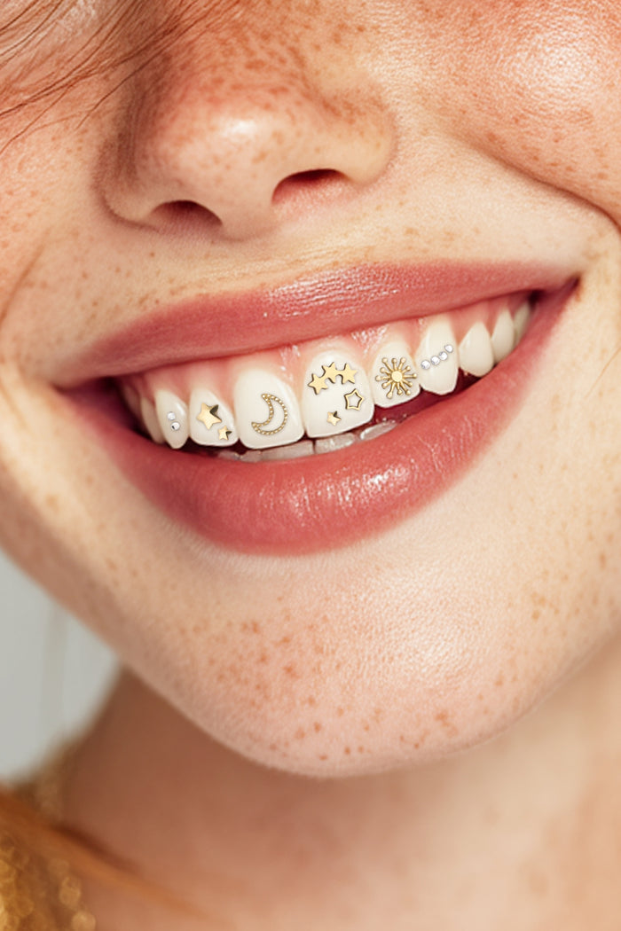 Close-up of a smiling mouth with celestial-themed tooth gems including moons, stars, and a sun.