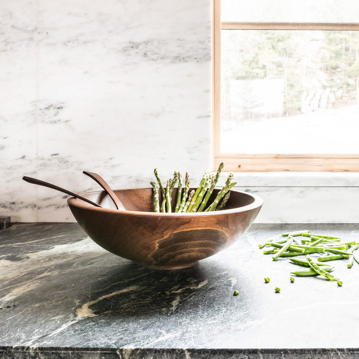 Dark wood bowl with two wooden spoons, containing fresh green beans on a marble countertop.