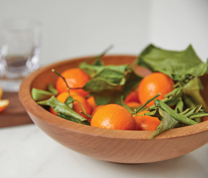 Cherry wood bowl filled with small tomatoes and green pods on a white surface.
