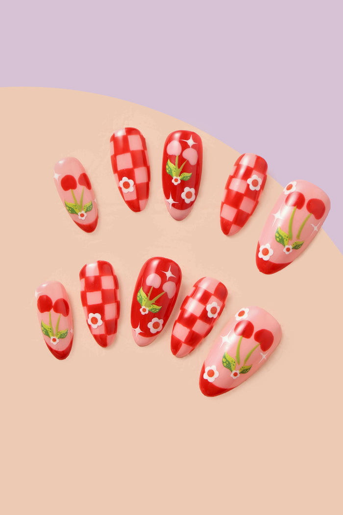 Red checkered and cherry-themed press-on nails with white flower accents.