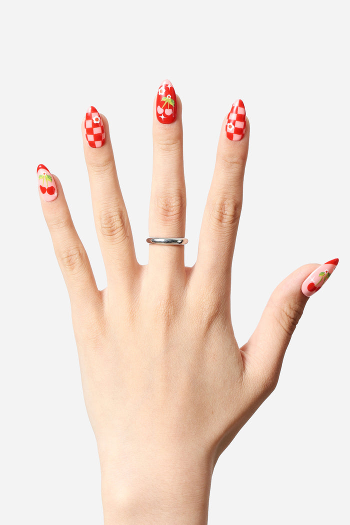 Hand modeling Checkered Cherries press-on nails with red and pink checkerboard and cherry designs.