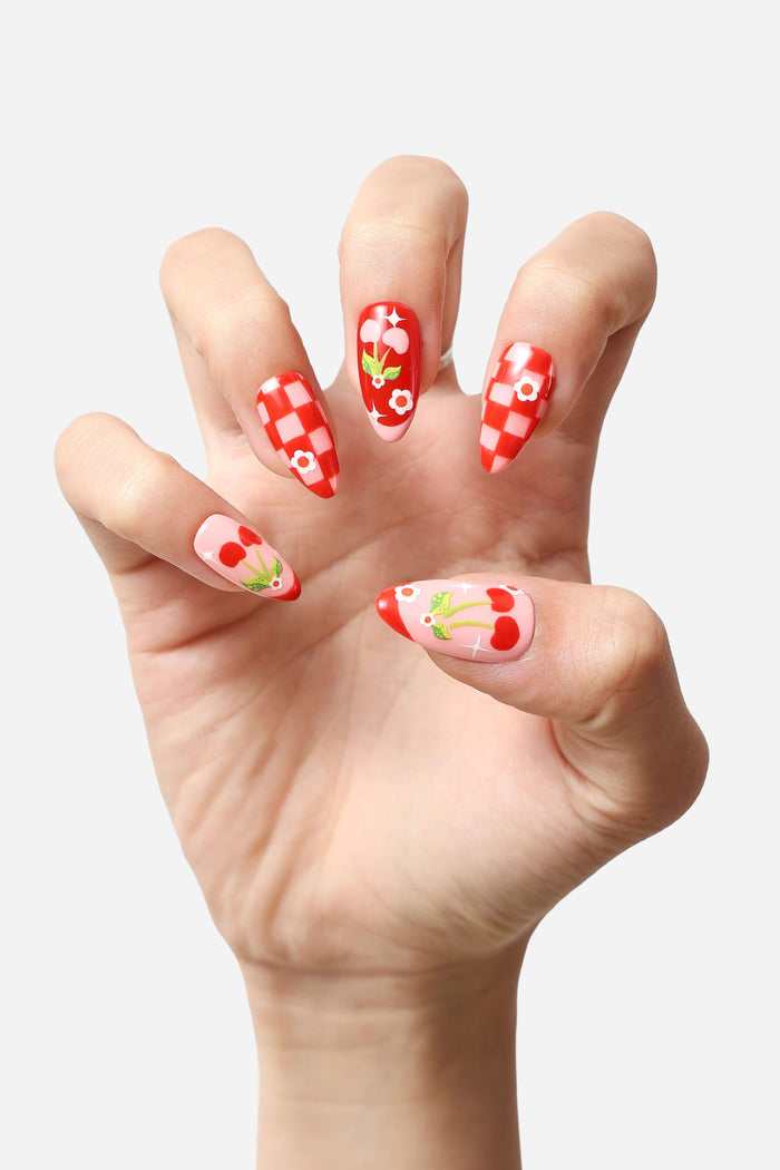 Hand displaying 'Checkered Cherries' press-on nails with red and white checkerboard pattern and cherry designs.