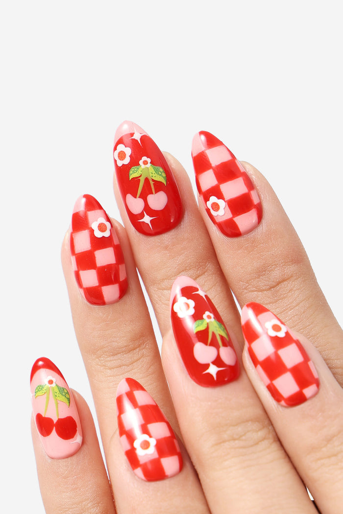 Press-on nails featuring a red checkerboard pattern and cherries with flowers, designed by Jess Miller.