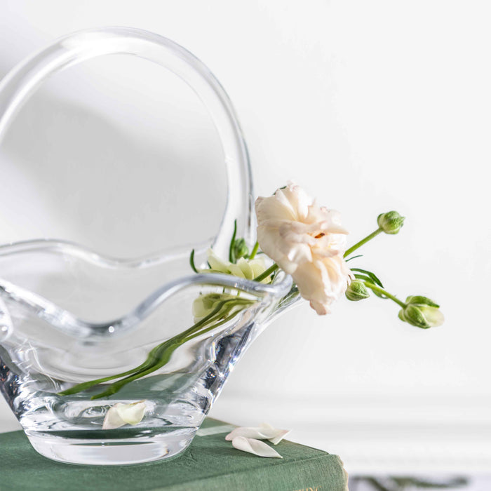 White ceramic basket-shaped vase tipped over with fresh carnation flowers and water spilling out.