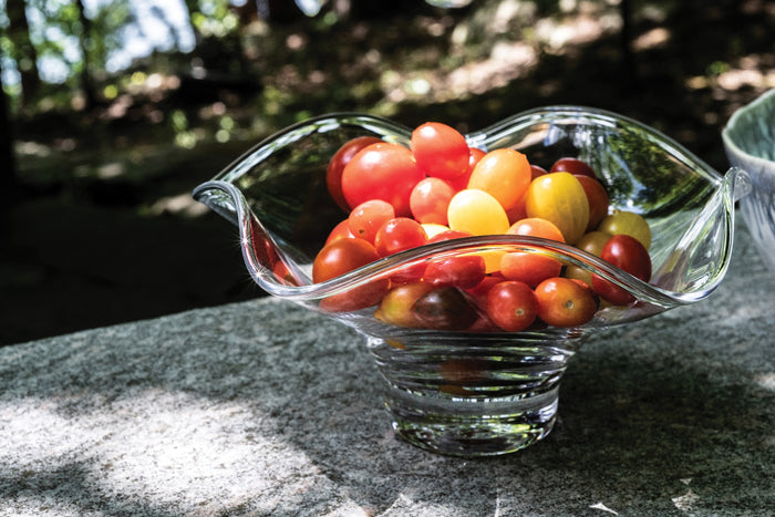 Clear glass bowl with wavy, flared rim holding red and yellow cherry tomatoes.