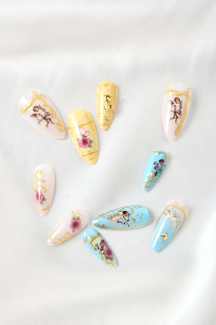 Almond press-on nails with cherub and floral rococo designs in pastel colors and gold accents.