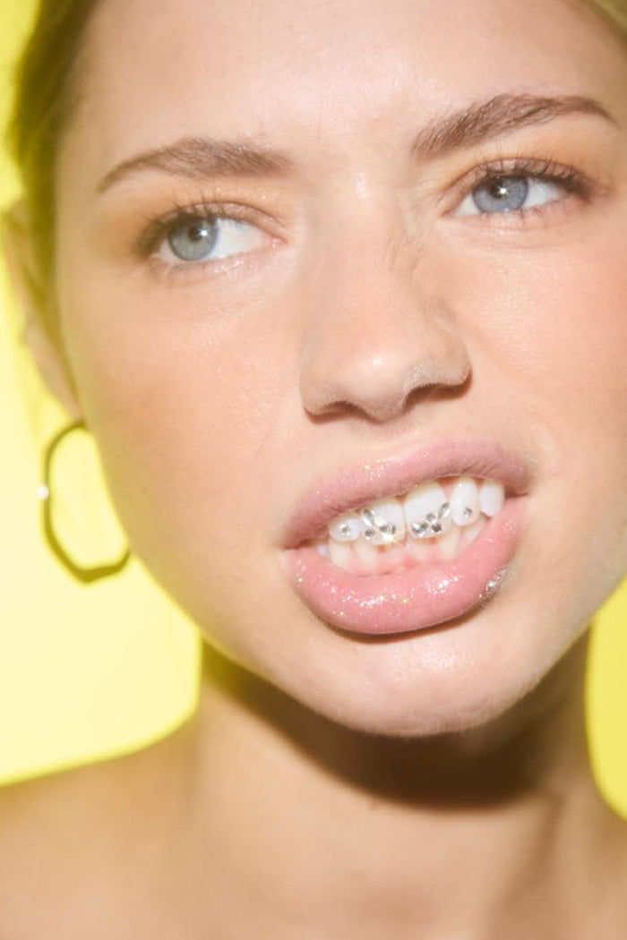 Close-up of woman's smile showing teeth with classic glam DIY tooth gems and glossy lips.