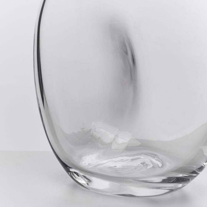 Clear glass carafe with curved, organic shape and dark rim, shown from side angle against white background.
