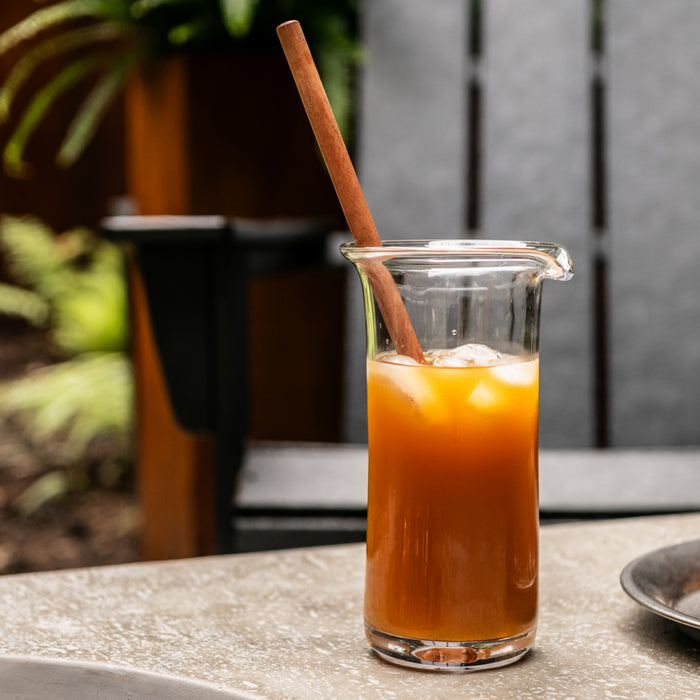 Brown wooden cocktail stirrer in a glass pitcher filled with amber liquid and ice.