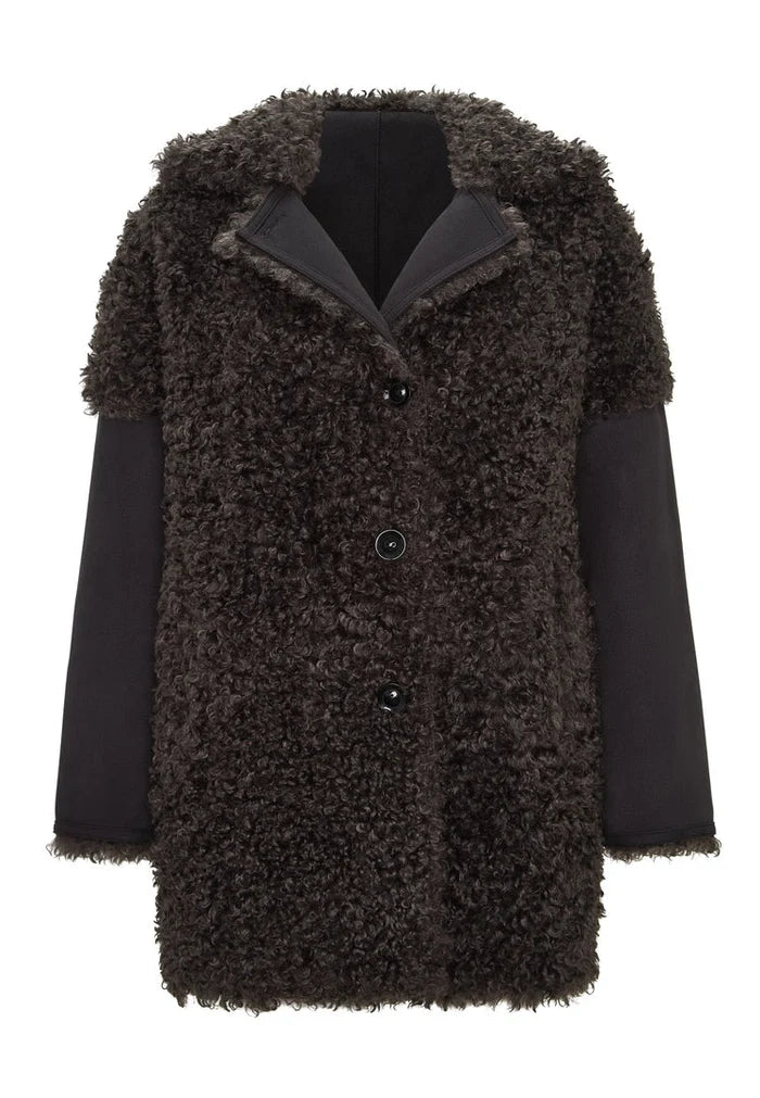 A stylish woman wearing a cozy black shearling Eva coat with a luxurious brown lining.