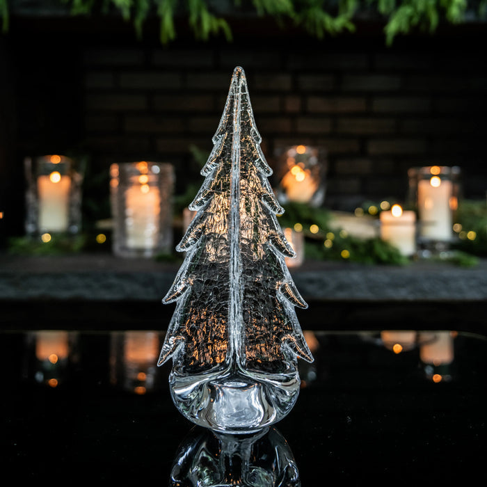 Clear glass crackle evergreen tree with textured surface and warm-toned interior, displayed with lit candles in background.