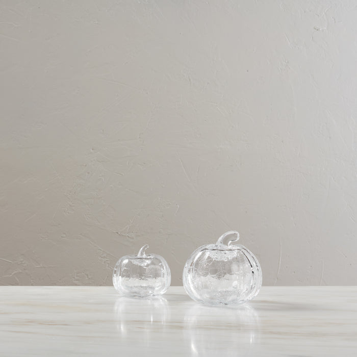Two clear glass pumpkins with textured crackle finish and stems displayed on a white surface.