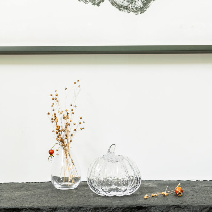 Clear glass pumpkin with crackle texture and stem, displayed next to dried botanicals in a vase.