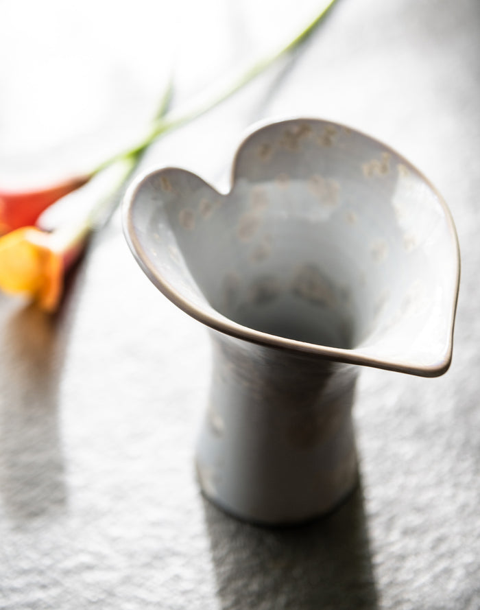White ceramic vase with curved calla lily petal shape and narrow cylindrical base, displayed with orange and yellow flowers.