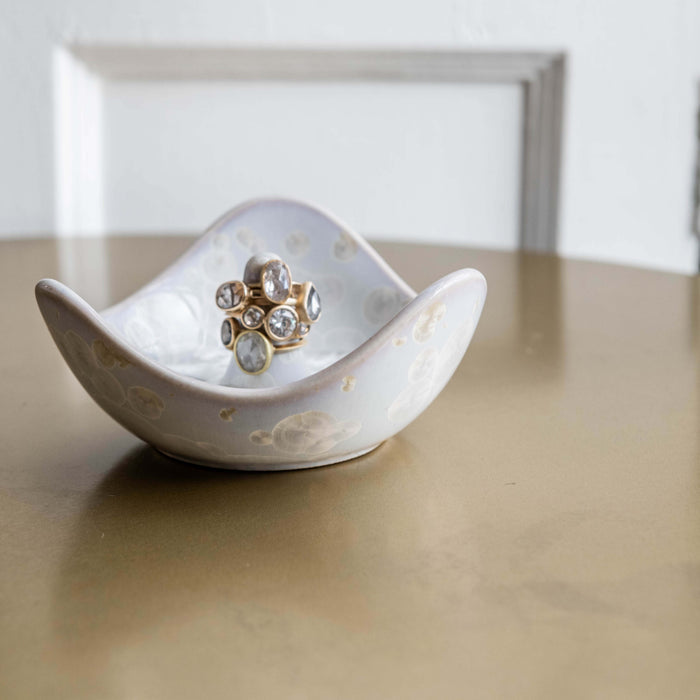 White crystalline ring holder with curved sides holding a gold-toned ring with clear stones, displayed with gift box in backg