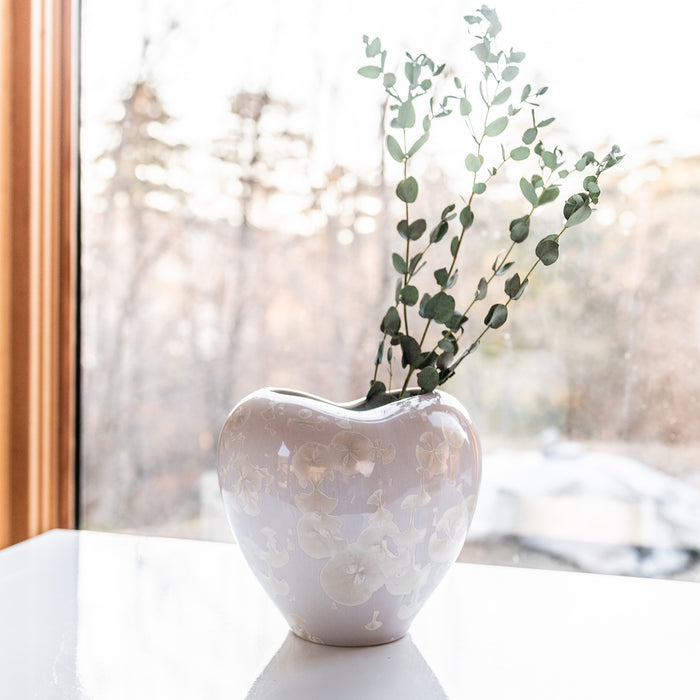 White heart-shaped vase with embossed floral pattern, holding green eucalyptus stems.