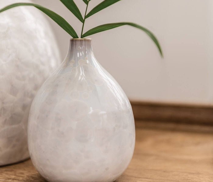 Translucent teardrop-shaped vase with frosted white finish holding green leafy stems.