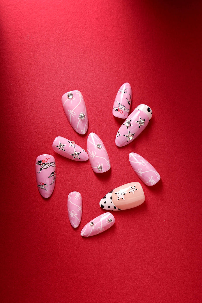 Pink almond press-on nails with Dalmatian dog and bow designs, accented with rhinestones.
