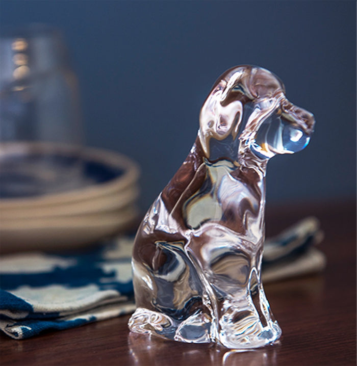 Clear glass dog figurine with brown and white coloring, sitting upright on a wooden surface.