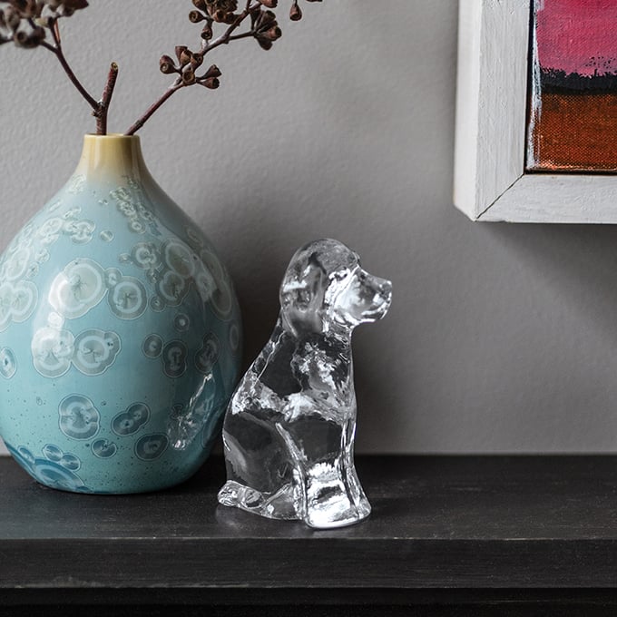Clear glass dog figurine sitting next to turquoise ceramic vase with dried branches.