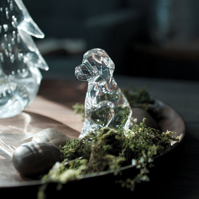 Clear glass dog figurine displayed on moss with decorative stones and crystalline elements.