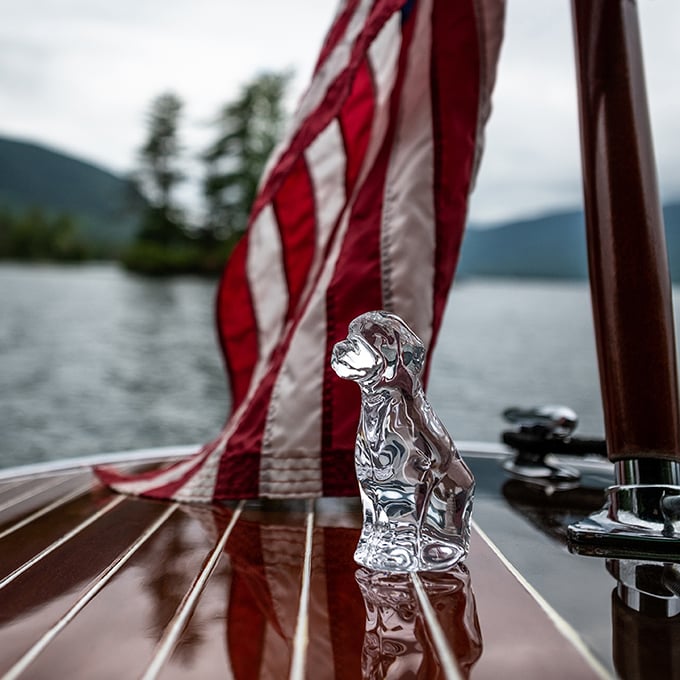 Silver dog figurine on boat deck with American flag and mountain lake in background.