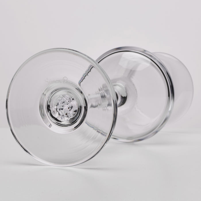 Two clear glass aperitif glasses with wide bowls and thin stems positioned at angles.