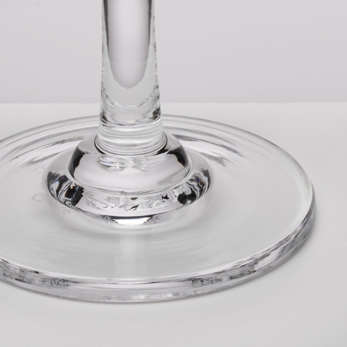 Clear glass aperitif glass with wide saucer base and tall stem on white surface.