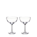 Two clear glass coupe glasses with stems and wide bowls on white background.