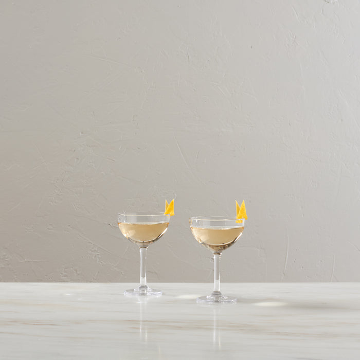 Two clear coupe glasses filled with pale yellow liquid and garnished with lemon twists.