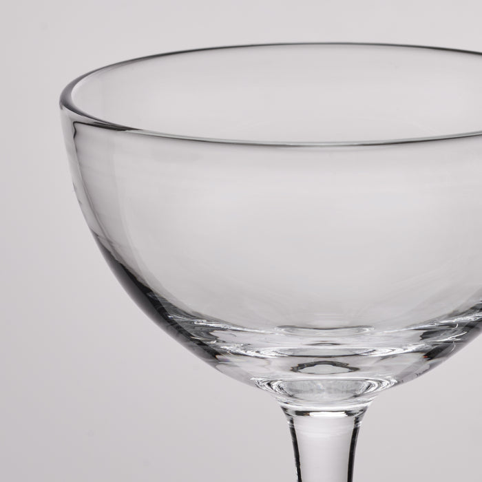 Clear glass coupe with wide bowl, thin stem, and dark rim detail against white background.