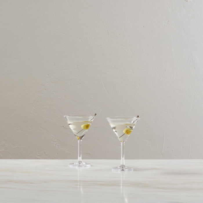 Two martini glasses filled with clear liquid and green olives on cocktail picks against a neutral background.